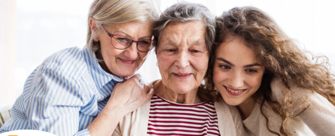Three generation embrace and look at a computer, representing the sandwich generation.