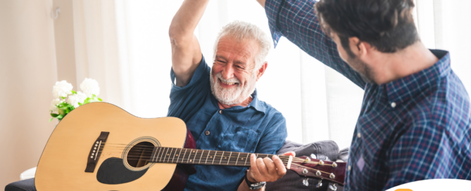 A smiling son high fives his happy elderly father as he plays the guitar, showing the positive effect music can have on people, including those with dementia.