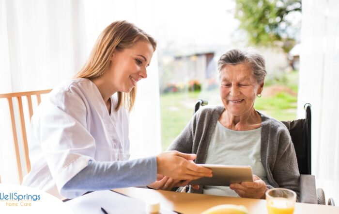 A professional caregiver smiles as she helps a happy senior client with her tablet, showing that she is managing caregiving stress well.